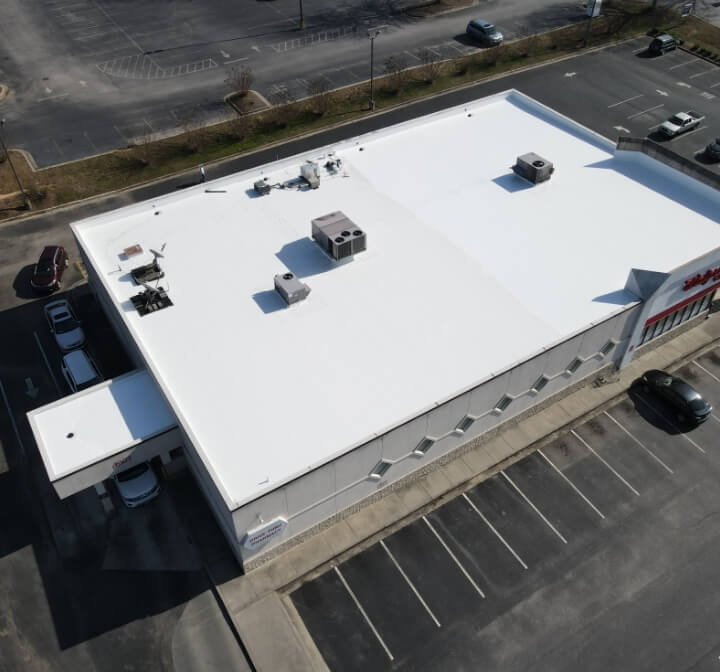 Aerial view of a white-roofed commercial building with a parking lot.