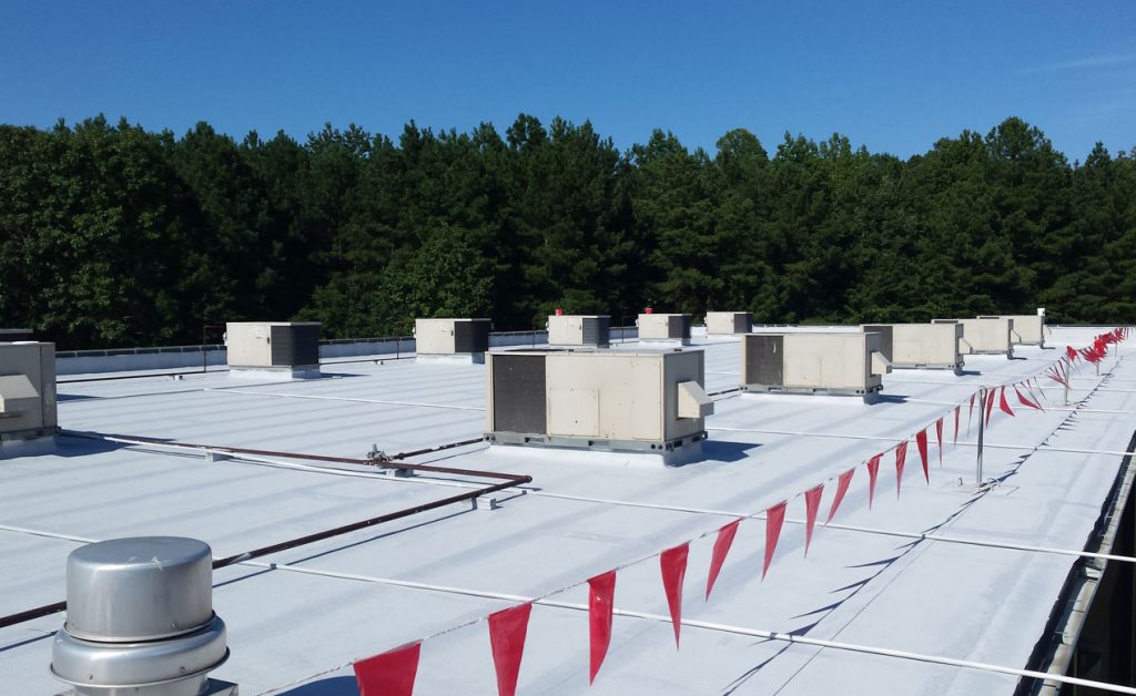 White flat rooftop with HVAC units and red safety flags under a clear blue sky.
