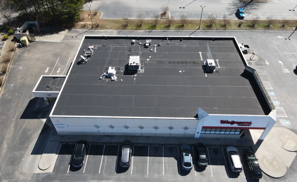 Aerial view of a commercial building with rooftop equipment and parked cars.