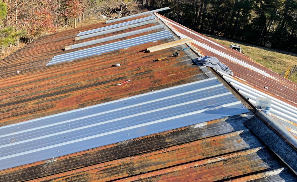 Roof with new metal panels partially installed over old wooden boards.
